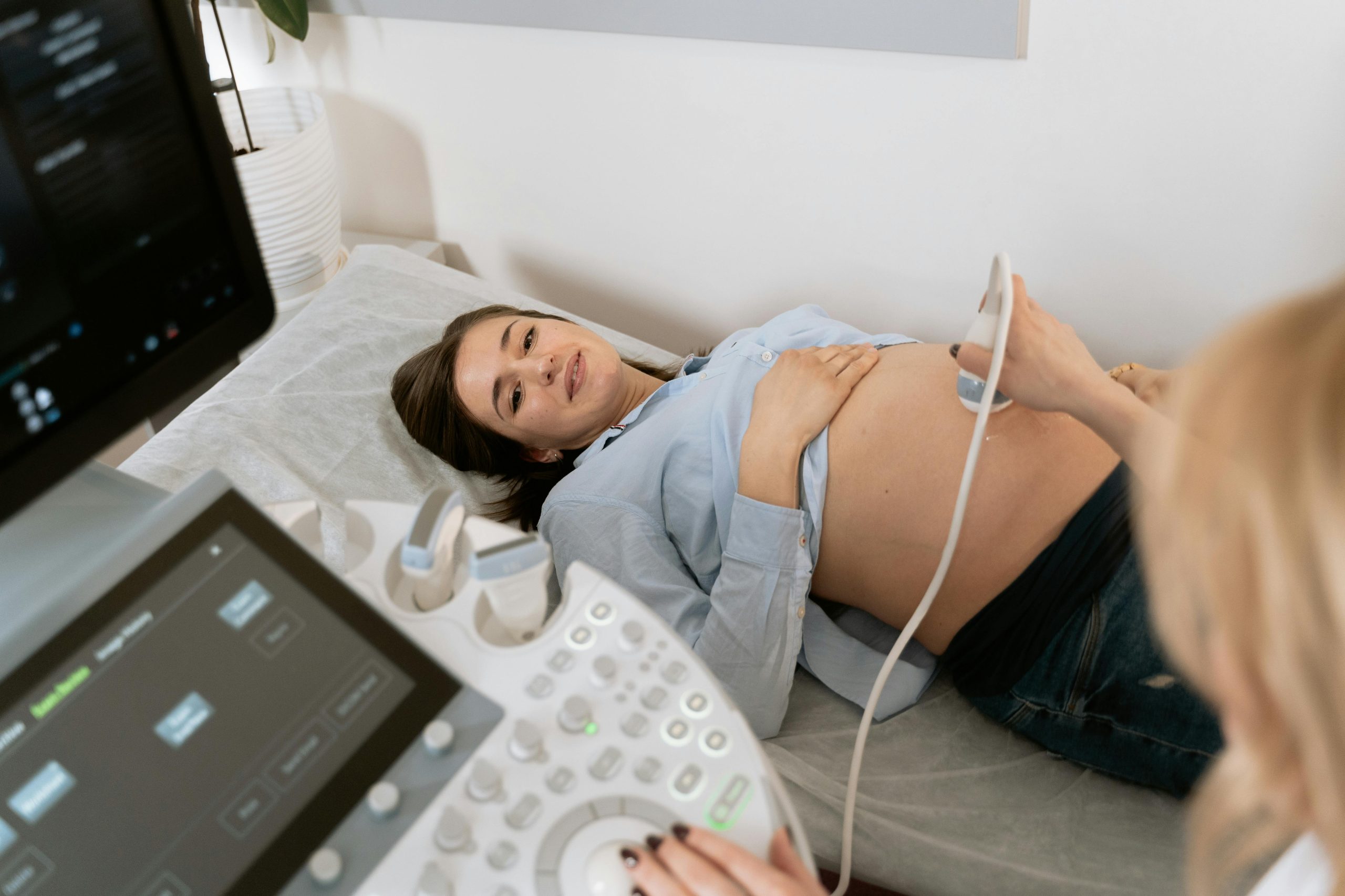 A woman lies on a bed as an ultrasound machine is used for pregnancy sonography in an OBS/GYNAE setting.